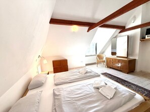 A bedroom with a sloped ceiling, a bed with white linens, a wooden dresser, a chair, and a large mirror. - Holiday Home in Oldsum With Swimming Pool (Oldsum)
