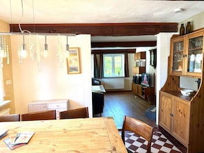 A dining area with a wooden table and chairs, a kitchen with wooden cabinets, and a window with curtains. - Holiday Home in Oldsum With Swimming Pool (Oldsum)