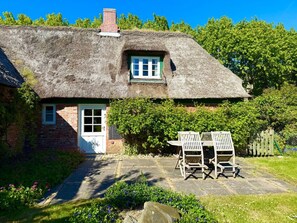 A traditional thatched-roof cottage with a small window, a brick door, and a stone pathway leading to a wooden bench. - Holiday Home in Oldsum With Swimming Pool (Oldsum)