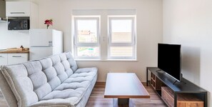 Un saló modern amb un sofà, una televisió, una taula petita i una zona de cuina amb un microones.