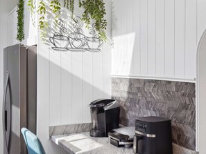 Cocina moderna con encimera de mármol, cafetera, báscula y decoración de planta en la pared.