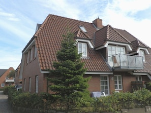 A two-story house with a tiled roof, a balcony, and a small tree in the front yard. - Holiday Apartment With 1 Bedroom (Wyk auf Foehr)
