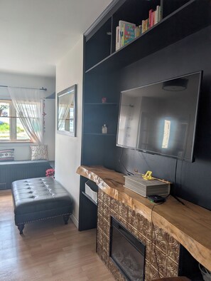 A modern living room with a flat-screen TV mounted on a dark wall, a wooden coffee table, a black leather sofa, and a bookshelf with books. - Gilbert Getaway | Charming 2-Bedroom 2-Bathroom | Downtown St. John’s Retreat 🏡 (St. John's)
