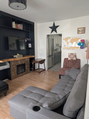 A modern living room with a grey sectional sofa, a flat-screen TV, a wooden coffee table, and a fireplace. - Gilbert Getaway | Charming 2-Bedroom 2-Bathroom | Downtown St. John’s Retreat 🏡 (St. John's)