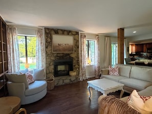 Una sala de estar con chimenea de piedra, un sofá, una mesa de centro y vistas al exterior.
