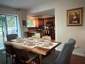 A dining area with a wooden table set for four, chairs, and a view of the kitchen in the background. - SEC Beauty Offers Outdoor Oasis & Entertaining! Gorgeous Yard & Privacy (Norman)