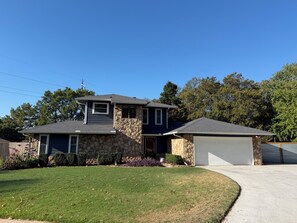 A two-story house with a stone facade, a garage, and a well-maintained lawn. - SEC Beauty Offers Outdoor Oasis & Entertaining! Gorgeous Yard & Privacy (Norman)
