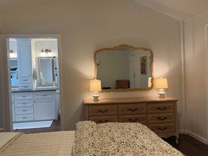 A bedroom with a bed, a dresser with drawers, a mirror, and a door leading to a bathroom. - SEC Beauty Offers Outdoor Oasis & Entertaining! Gorgeous Yard & Privacy (Norman)
