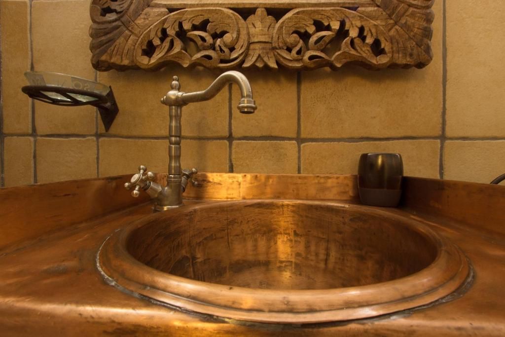 Un lavamanos de cobre con un solo grifo y un panel de madera decorativo encima.