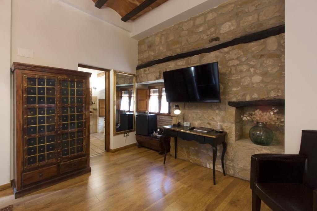 Quarto com parede de pedra, televisão de tela plana acima de uma lareira, armário de madeira e escrivaninha com abajur.