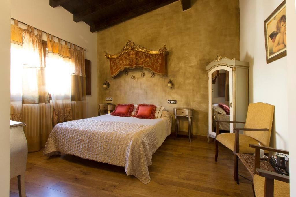 Quarto com cama grande, piso de madeira, cabeceira decorativa, uma cadeira e mesa de cabeceira.