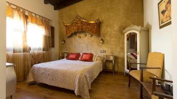 Quarto com cama grande, piso de madeira, cabeceira decorativa, uma cadeira e mesa de cabeceira.