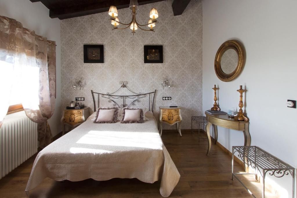 A bedroom with a large bed, a chandelier, a bedside table with a lamp, and a mirror on the wall.