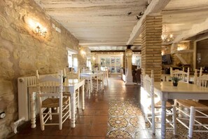 Interno di un ristorante con pareti in pietra, sedie di legno e pavimento a disegno.