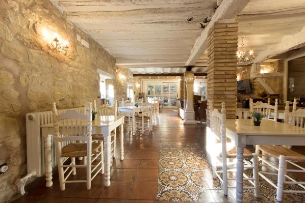 A restaurant interior with stone walls, wooden chairs, and a patterned floor.