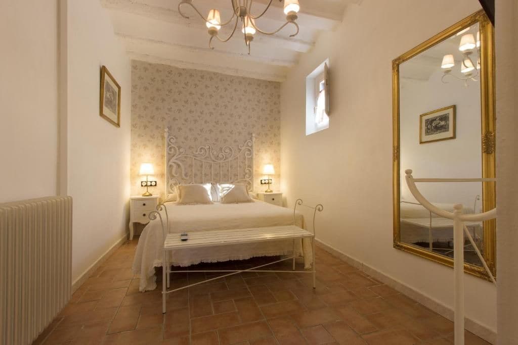 A bedroom with a bed, bedside lamps, a radiator, a mirror, and a chandelier.