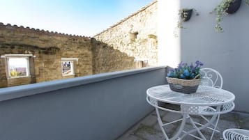 A balcony with a white metal table and chairs, a wicker basket with flowers, and a stone wall in the background.