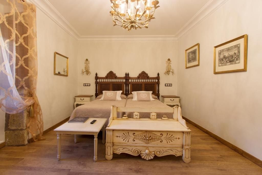 A bedroom with a large bed, bedside tables, a chandelier, and framed artwork on the walls.