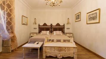 A bedroom with a large bed, bedside tables, a chandelier, and framed artwork on the walls.