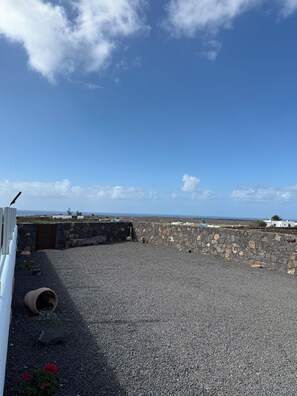 En takterrass med en stenmur, ett grusunderlag och utsikt över havet.