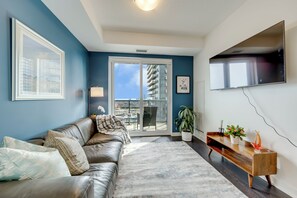 Uma sala de estar moderna com sofá de couro, televisão de tela plana, varanda com vista para a cidade e um vaso de planta.