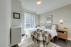 A bedroom with a bed, bedside tables, a nightstand, a lamp, a picture on the wall, and a window with curtains. - Fully furnished executive suite near Square One in the heart of Mississauga. (Mississauga)