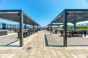 An outdoor patio area with tables and chairs under metal canopies, a grill station, and a view of the cityscape. - Fully furnished executive suite near Square One in the heart of Mississauga. (Mississauga)