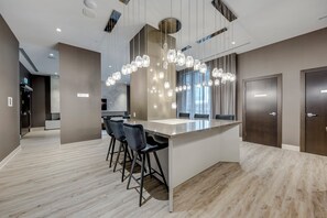 Cozinha moderna com ilha central, banquetas, iluminação pendente e vista para o exterior por grandes janelas.