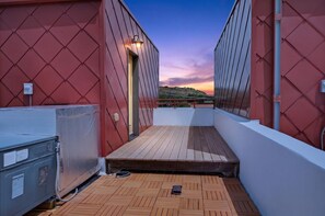 A covered outdoor deck with a wooden floor, a metal container, and a wall with a diamond-patterned design. - Rick's Chill Pad for 4 - Chic Downtown Billings Retreat (Billings)