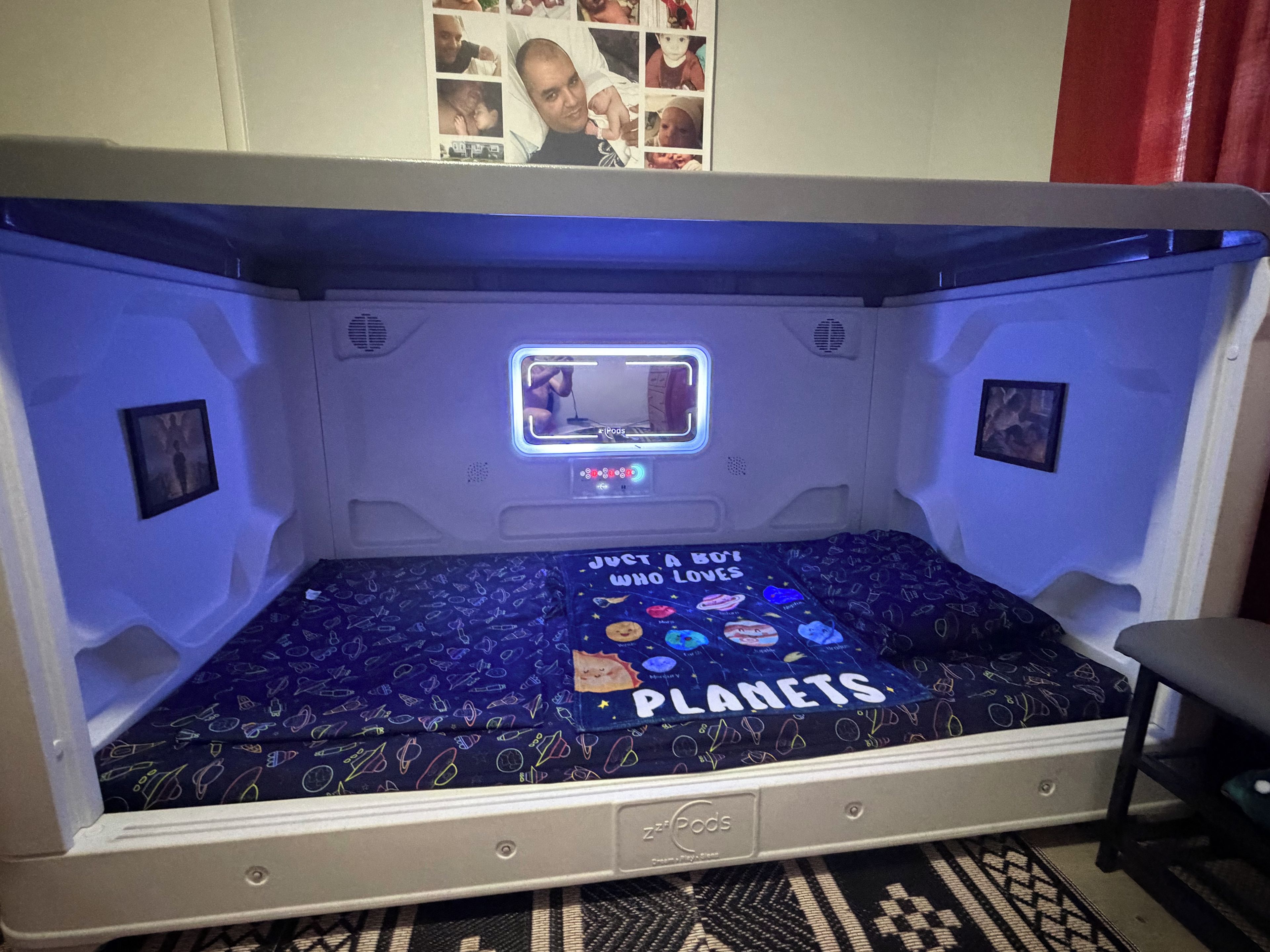Un letto a castello con lettore portatile integrato, una galleria di foto appesa al muro e copripiumino con motivo spaziale.