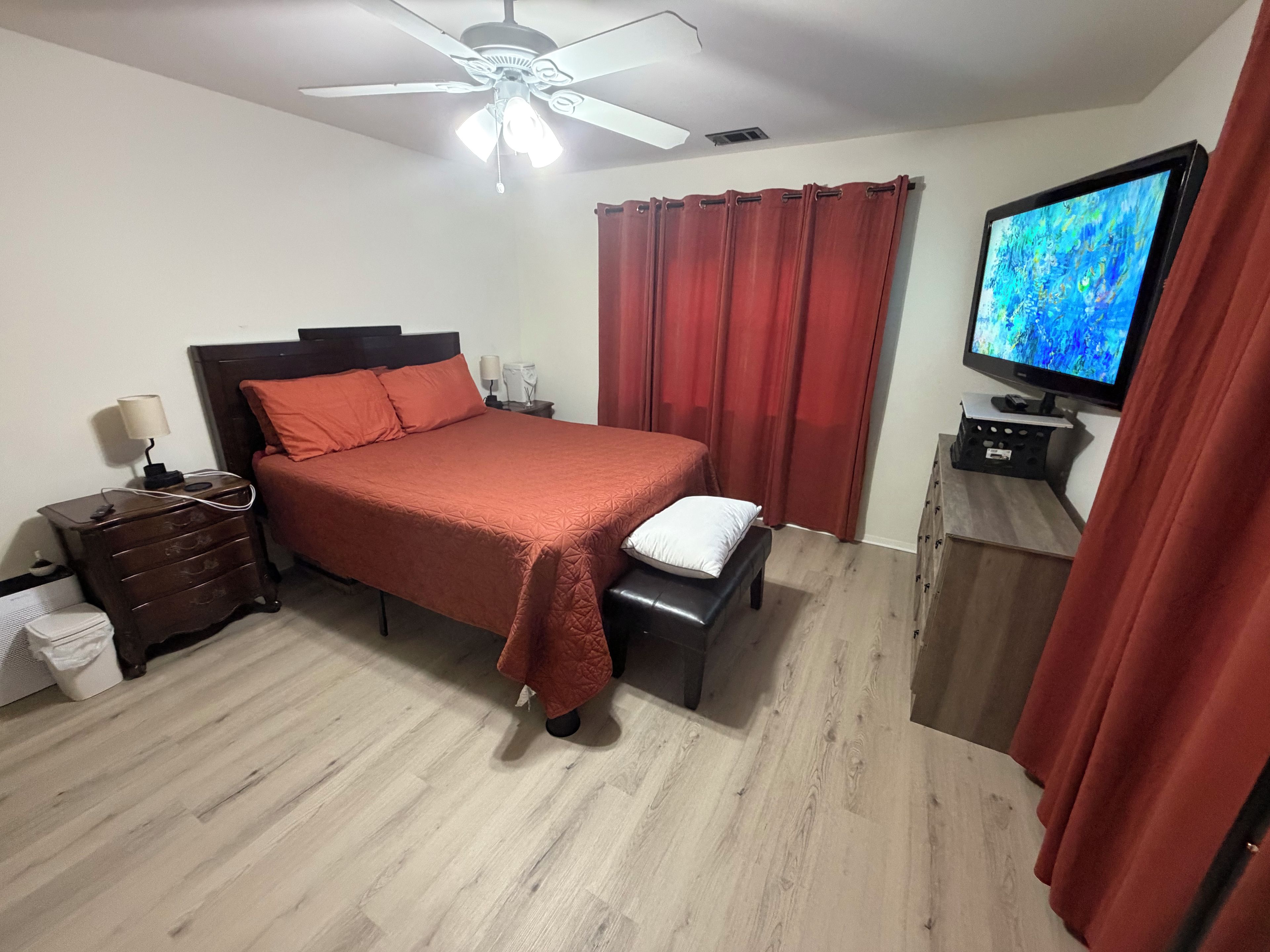 A bedroom with a bed, a nightstand, a TV, and a ceiling fan.