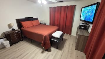 A bedroom with a bed, a nightstand, a TV, and a ceiling fan.