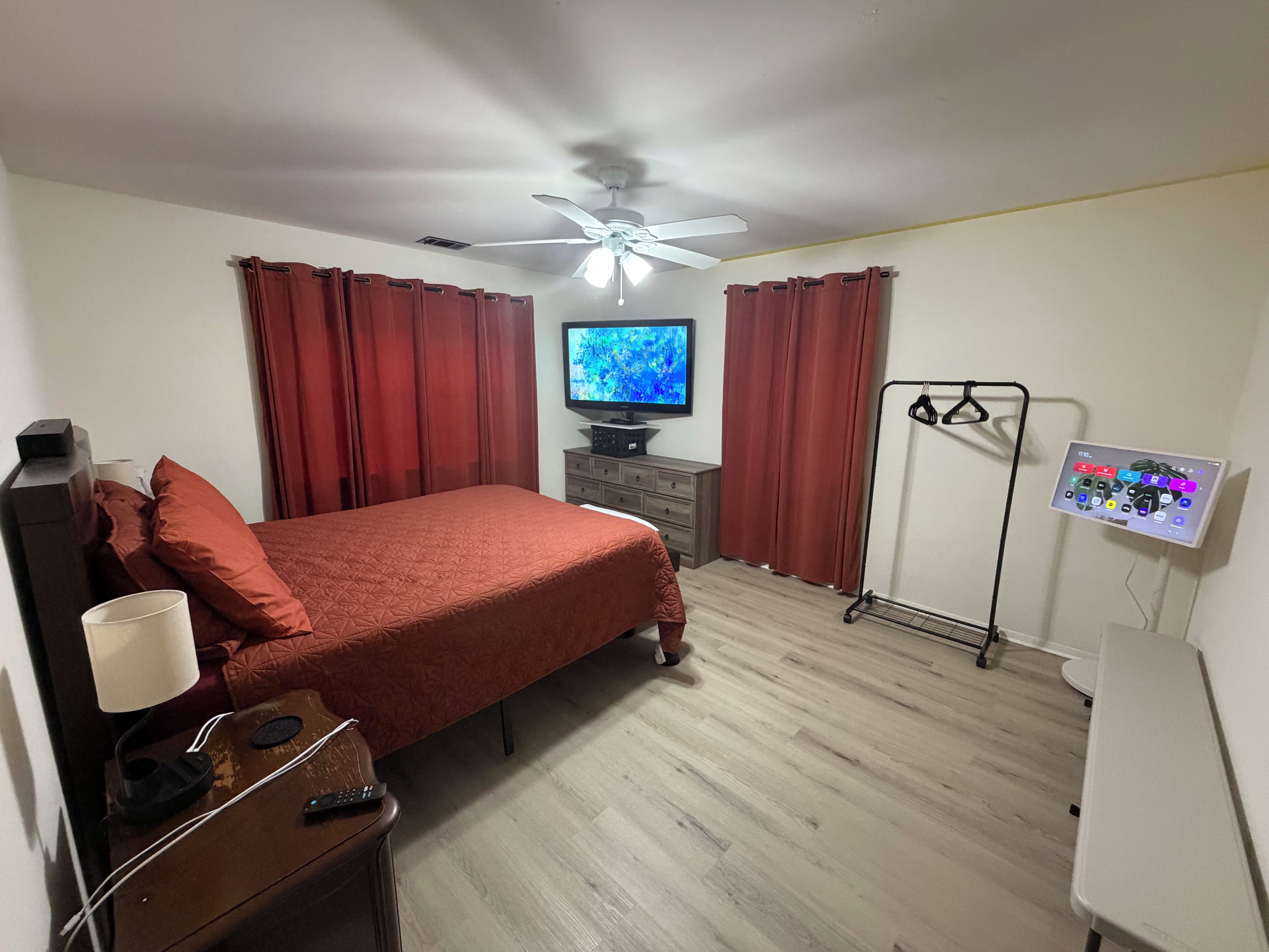 A bedroom with a bed, a television, a ceiling fan, a dresser, and a wall-mounted charging station.