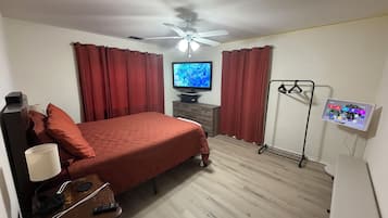 A bedroom with a bed, a television, a ceiling fan, a dresser, and a wall-mounted charging station.