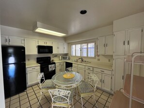 A compact kitchen with white cabinets, a black refrigerator, a microwave, a stove, and a dining area with a round table and chairs. - Quiet Scottsdale location for Snowbirds - near golf, restaurants and more. (Scottsdale)