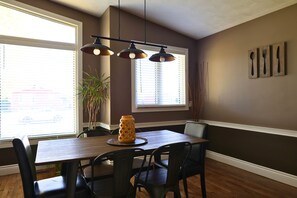 A dining area with a wooden table, black chairs, pendant lights, and a vase on the table. - Melrose Heights | 4BR Executive Home (Timmins)