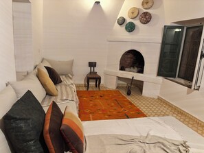 A cozy living room with a sofa, a patterned rug, a fireplace, and decorative plates on the wall. - Luxury Moroccan Riad with Private Pool & Rooftop Terrace (Essaouira)
