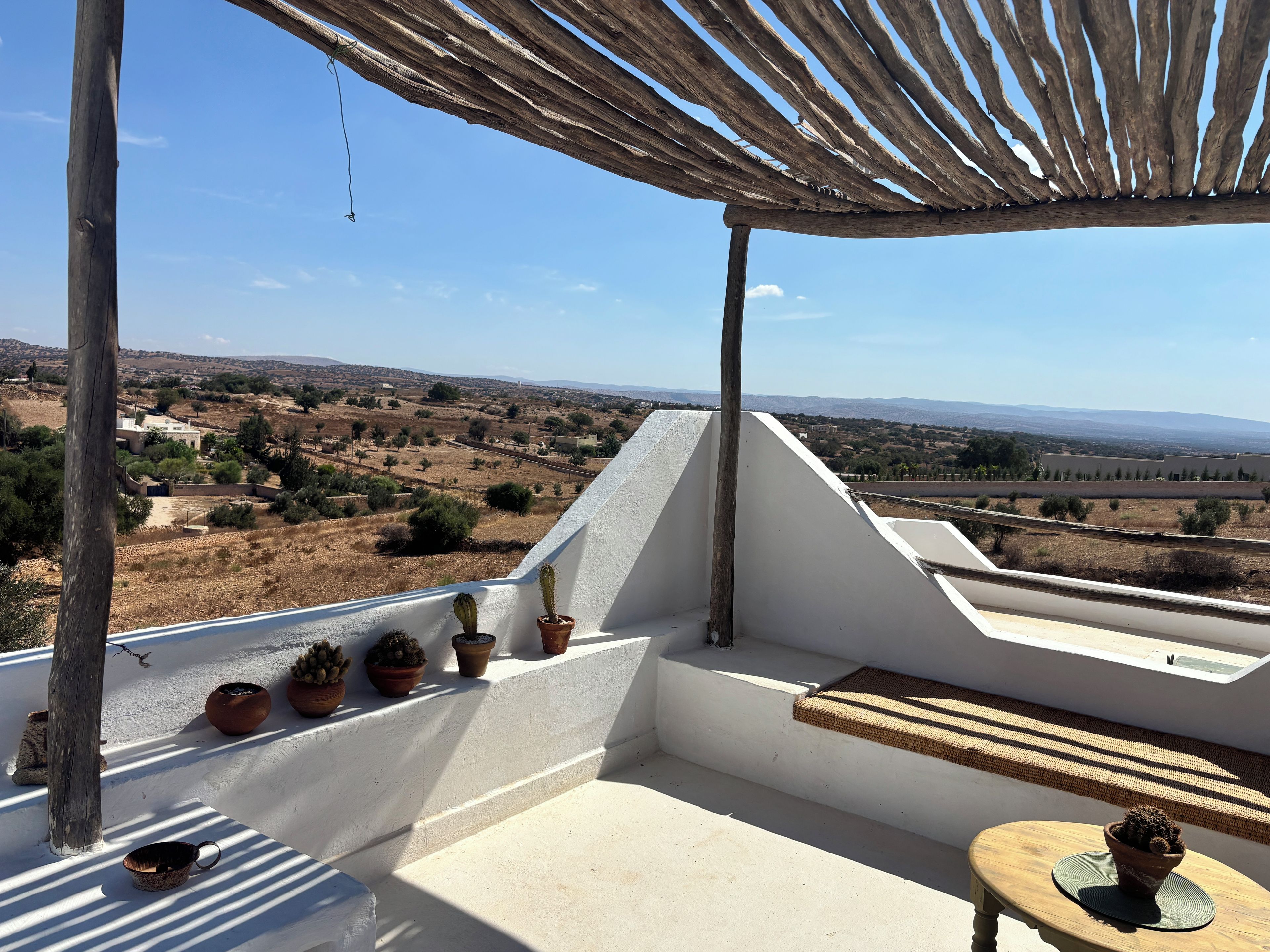 Ein Balkon mit Blick auf eine ländliche Landschaft, Topfpflanzen und einem Holztisch.