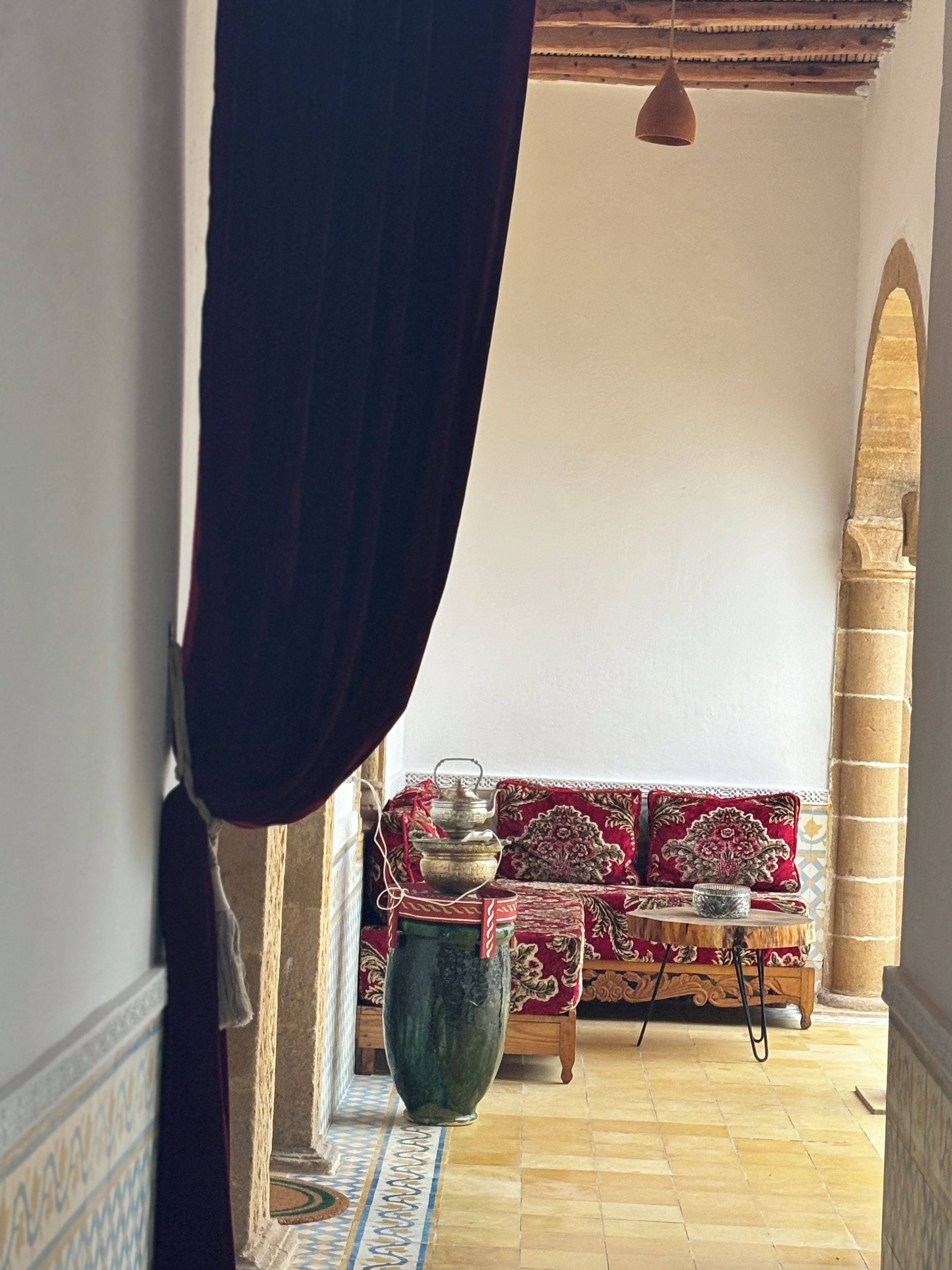 Ein Zimmer mit einer gemusterten Couch, einer großen Vase und einem gefliesten Boden.
