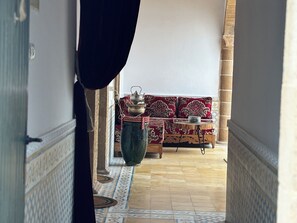 A corridor with a patterned floor leading to a seating area with a sofa and a table, a large vase, and a decorative bowl. - Luxury Moroccan Riad with Private Pool & Rooftop Terrace (Essaouira)