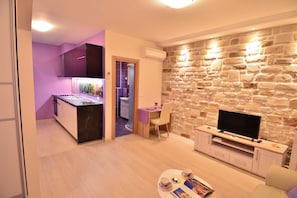 Un soggiorno moderno con una parete a parete in pietra, una TV a schermo piatto e un'area da pranzo con un tavolo viola.