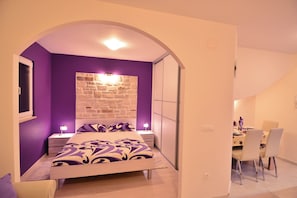 A bedroom with a bed, a nightstand, a dresser, a dining area with chairs, and a staircase. - Cozy 1-bedroom apartment in Dubrovnik with AC, and private parking place (Dubrovnik)