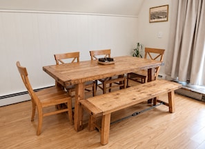 A wooden dining table with four chairs and a bench, set against a white wall with a framed picture. - Penney Pines: A Cozy Catskills A-Frame (Catskill)