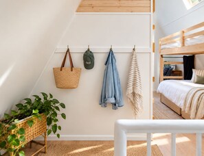 A cozy attic bedroom with a bunk bed, a hanging laundry rack, and a wicker plant. - Penney Pines: A Cozy Catskills A-Frame (Catskill)