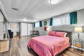 Un dormitorio con cama, escritorio, silla, ventana con cortinas, puerta y espejo instalado en la pared.