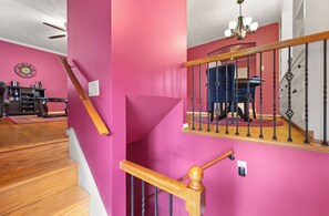 A staircase with a wooden handrail and black balusters, leading to a room with a red wall and a chandelier. - Pink Paradise in Silver Spring Suburbs (Silver Spring)