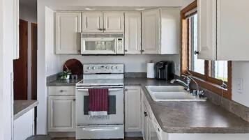 A compact kitchen with white cabinets, a built-in oven, a microwave, a sink, and a window.