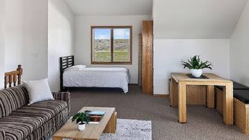 A bedroom with a bed, a window with a view of a field, a wooden headboard, and a bedside table with a plant.