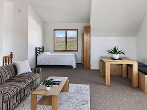 A bedroom with a bed, a window with a view of a field, a wooden headboard, and a bedside table with a plant. - Peaceful & Private 2 Bed West End Home on a Gated Acre (Billings)