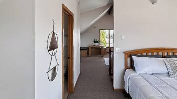 A bedroom with a wooden headboard, a bed with white bedding, a carpeted floor, and a hallway leading to a dining area.